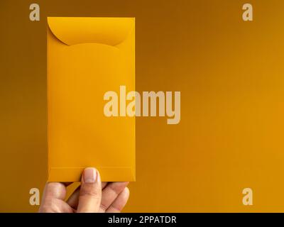 Hand mit goldenem Umschlag, vertikal, isoliert auf gelbem Hintergrund mit Kopierbereich. Hongbao-Paket für Glücksgeld in chinesischem Mond, neu Stockfoto