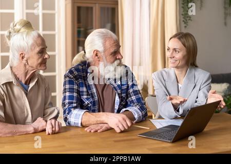 Finanzberater, der ein Notebook verwendet und dem älteren Paar während seines Meetings zu Hause die finanzielle Kompetenz erklärt Stockfoto