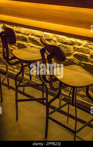 Barhocker, Stühle in einer Bar mit künstlichem Licht und einer mit Ziegeln bedeckten Bar Stockfoto