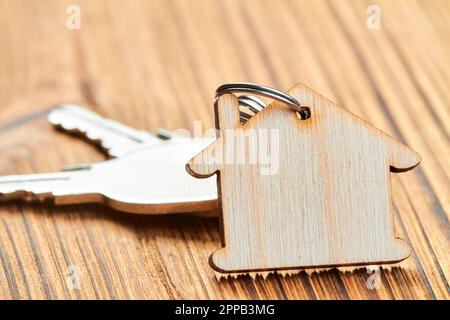 Schmuckkette in Form eines Holzhauses mit den Schlüsseln zur Wohnung auf Holzhintergrund Stockfoto