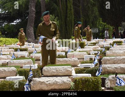 Jerusalem, Israel. 02. Februar 2014. Israelische Soldaten setzen Nationalflaggen mit schwarzen Schleifen auf die Gräber gefallener Soldaten am Mt. Herzl Militärfriedhof in Jerusalem am Sonntag, den 23. April 2023. Israel wird am 24. April den Gedenktag für Soldaten und Terroropfer bei Sonnenuntergang begehen. Foto von Debbie Hill/ Kredit: UPI/Alamy Live News Stockfoto