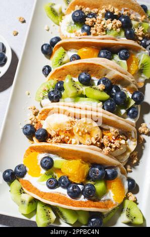 Taco Pfannkuchen mit frischem Obst, Blaubeeren und Joghurt Füllung, gesundes Frühstück oder Snack auf hellem Hintergrund Stockfoto