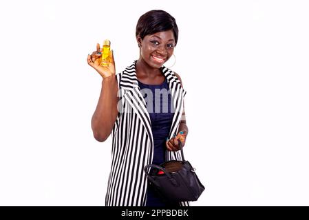 Porträt einer schönen jungen Frau, die eine kleine Flasche Parfüm zeigt, während sie in die Kamera lächelt. Stockfoto