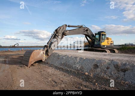 Der große gelbe Hydraulikbagger bewegt die Erde auf der Baustelle unten am Hafen. Stockfoto