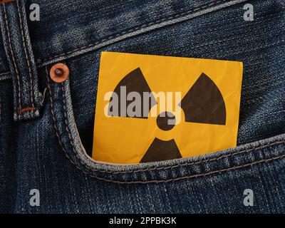 Ein Strahlungswarnschild, das aus einer Jeanstasche ragt. Schließen. Stockfoto