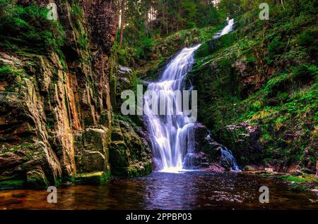 Bezaubernder Wasserfall in den Bergen zwischen Felsen und grünen Pflanzen. Der berühmte Kamienczyk-Wasserfall im Karkonosze-Nationalpark, Polen. Stockfoto
