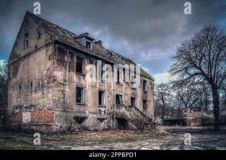 Altes, zerstörtes Gebäude in einer dunklen Landschaft. Das linkes einstürzendes Haus, das Objekt, das in den Ruin fällt, wird wahrscheinlich von Obdachlosen bewohnt. Stockfoto