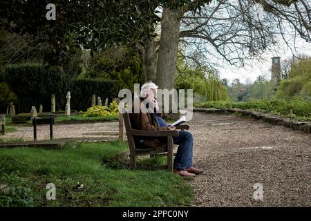 Der Senior sitzt allein auf einer Bank und liest draußen ein Buch. England Großbritannien Stockfoto