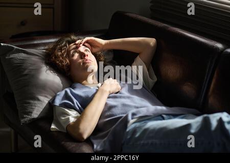 Gestresste junge Frau, die den Kopf auf dem Kissen hält, während sie auf einer bequemen schwarzen Ledercouch liegt und ihre Probleme einem Psychologen beschreibt Stockfoto