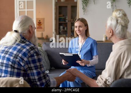 Junge, die während ihres Heimbesuchs mit dem Seniorenpaar sprach und die Krankenversicherungskarte ausfüllte Stockfoto