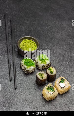 Sushi mit Gurke und grünen Algen. Essensstäbchen. Wasabi in einer schwarzen Schüssel. Speicherplatz kopieren. Draufsicht. Schwarzer Hintergrund Stockfoto