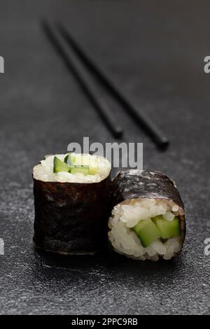 Sushi mit Gurke in Nori-Blättern. Essensstäbchen. Schließen. Speicherplatz kopieren. Schwarzer Hintergrund Stockfoto