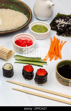 Essensstäbchen. Sushi mit Kaviar. Ingwer und Wasabi in Schüsseln. Sojasoße in einer Schüssel und Reis auf einem Teller. Weißer Hintergrund. Stockfoto