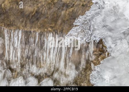 Ein malerischer Blick auf einen kleinen Wasserfall, der über zerklüftete Felsen stürzt, bedeckt mit einer Schicht frostigen Schnees Stockfoto