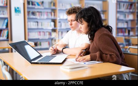 Asiatische Schülerin mit Klassenkamerad Kerl, studieren auf einem Laptop und Notizen in einem Copybook Stockfoto