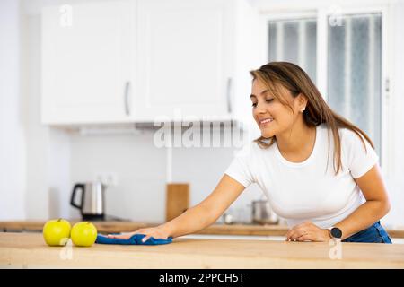 Lächelnde junge hispanische Frau, die zu Hause Küchenoberflächen abwischt Stockfoto