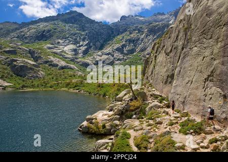 Blick auf die Gipfel des Restonica-Gebirges und einen Wanderweg, auf dem eine junge Frau mit einem Hund läuft, Lac du Melu, Korsika, Frankreich Stockfoto