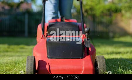 Rasenmäher mäht grünes Gras im Garten. Mann mäht mit elektrischem Rasenmäher im Garten. Zeitlupe. Männlicher Arbeiter, der im Hof läuft Stockfoto