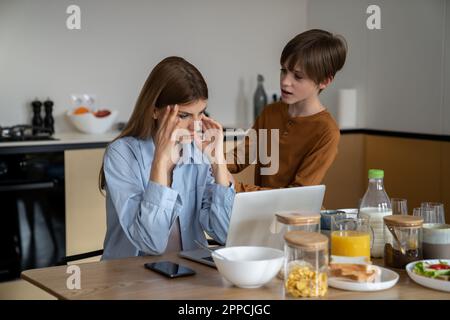 Freiberufliche Mutter, die mit einem Kind von zu Hause aus arbeiten will, schaut auf den Laptop-Bildschirm und versucht, sich zu konzentrieren Stockfoto