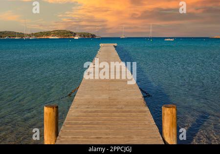 Malerischer Blick auf das blaue Meer und eine lange hölzerne Anlegestelle bei Sonnenuntergang am Strand von Rondinara, Insel Korsika, Frankreich Stockfoto