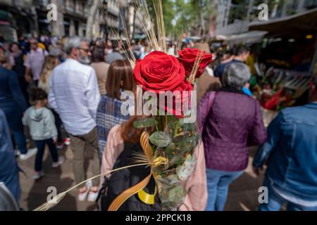 Barcelona, Spanien. 23. April 2023. Eine Frau trägt rote Rosen auf dem Rücken entlang der Las Ramblas in Barcelona. Katalonien feiert am 23. April jährlich den Tag von Sant Jordi, das traditionelle Buch- und Rosenfest. Die Straßen sind voller Verkaufsstände, die Bücher und Rosen verkaufen. Kredit: SOPA Images Limited/Alamy Live News Stockfoto