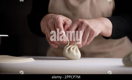 Nahaufnahme, Hände Formen Khinkali. Khinkali-Kochvorgang aus nächster Nähe. Küchenchefe Formen Khinkali. Lavash für Khinkali. Stockfoto