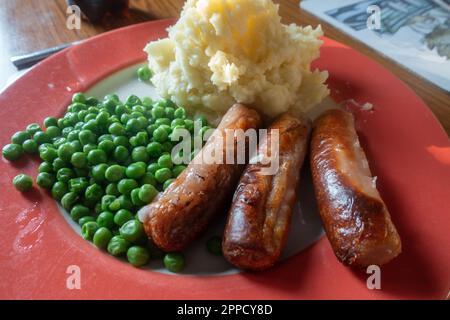 Würstchen, Kartoffelpüree und Erbsen auf einem roten Teller, Trostessen zum Abendessen. Stockfoto