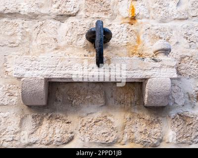 Rab, Kroatien - 24. August 2022: Ein alter, in Marmor gegossener Metallring ruht auf einem Steinregal, eingebettet in eine alte Wand mit komplizierter Architektur. Stockfoto