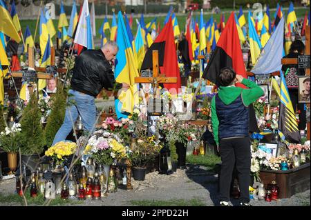 Lemberg, Ukraine 23. April 2023. Menschen stehen auf Gräbern auf dem Marsfeld des Friedhofs Lychakiv. Helden der Ukraine, Soldaten, die das Territorium der Ukraine verteidigten, sind hier begraben. Russland marschierte am 24. Februar 2022 in die Ukraine ein und löste damit den größten militärischen Angriff in Europa seit dem Zweiten Weltkrieg aus Stockfoto