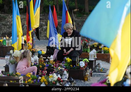 Lemberg, Ukraine 23. April 2023. Menschen stehen auf Gräbern auf dem Marsfeld des Friedhofs Lychakiv. Helden der Ukraine, Soldaten, die das Territorium der Ukraine verteidigten, sind hier begraben. Russland marschierte am 24. Februar 2022 in die Ukraine ein und löste damit den größten militärischen Angriff in Europa seit dem Zweiten Weltkrieg aus Stockfoto