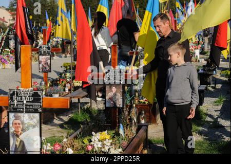 Lemberg, Ukraine 23. April 2023. Menschen stehen auf Gräbern auf dem Marsfeld des Friedhofs Lychakiv. Helden der Ukraine, Soldaten, die das Territorium der Ukraine verteidigten, sind hier begraben. Russland marschierte am 24. Februar 2022 in die Ukraine ein und löste damit den größten militärischen Angriff in Europa seit dem Zweiten Weltkrieg aus Stockfoto