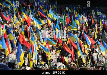 Lemberg, Ukraine 23. April 2023. Menschen stehen auf Gräbern auf dem Marsfeld des Friedhofs Lychakiv. Helden der Ukraine, Soldaten, die das Territorium der Ukraine verteidigten, sind hier begraben. Russland marschierte am 24. Februar 2022 in die Ukraine ein und löste damit den größten militärischen Angriff in Europa seit dem Zweiten Weltkrieg aus Stockfoto