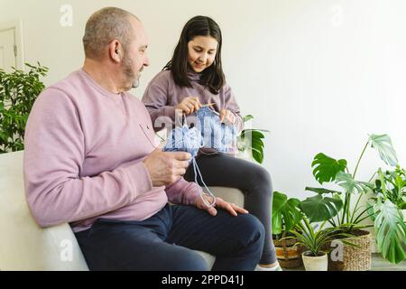 Lächelnder Senior-Mann, der Enkelin beim Stricken von Pullover zu Hause hilft Stockfoto