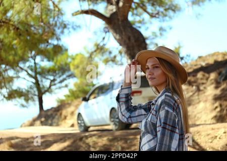 Rücksichtsvolle junge Frau mit Hut, die vor dem Auto steht Stockfoto