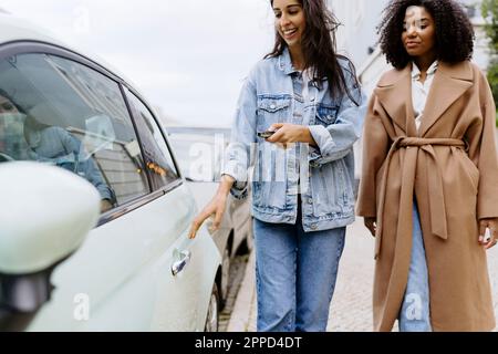 Glückliche junge Frau mit Freund, die das Auto mit der Schlüsselfernbedienung entriegelt Stockfoto