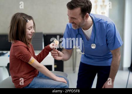 Glücklicher reifer Arzt, der dem Mädchen in der Klinik Lollipop gibt Stockfoto