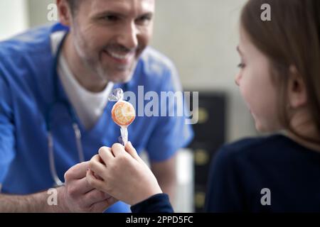 Glücklicher Arzt, der dem Mädchen in der Klinik Lollipop gibt Stockfoto