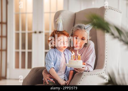 Ein Junge mit Großmutter bläst Kerzen auf Geburtstagskuchen zu Hause Stockfoto