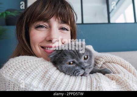 Lächelnde Frau umarmt Katze zu Hause Stockfoto