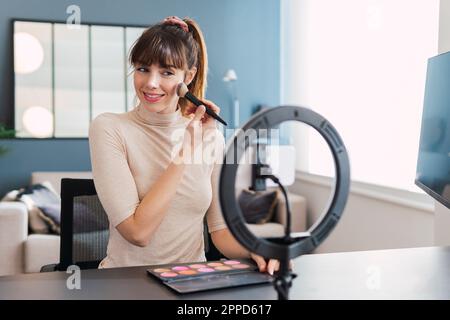 Lächelnder Vlogger, der zu Hause Make-up aufträgt und Tutorial macht Stockfoto