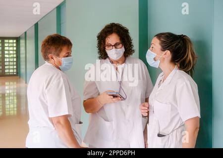 Krankenschwestern tragen Gesichtsschutzmasken, die im Krankenhaus miteinander reden Stockfoto