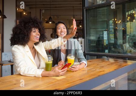 Eine glückliche Frau winkt von einer Freundin, die im Café sitzt Stockfoto