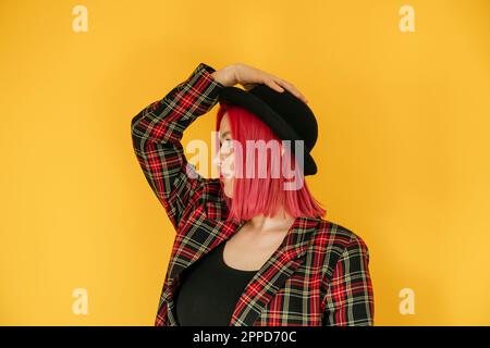 Rücksichtsvolle Frau mit Bowler-Hut, die vor gelbem Hintergrund steht Stockfoto