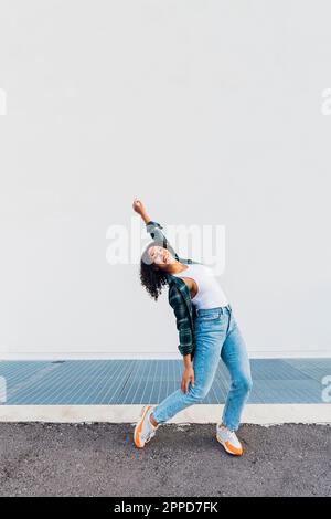 Lächelnde junge Frau, die vor der weißen Wand tanzt Stockfoto