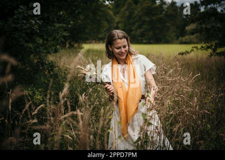 Lächelnde Frau mit Wildblumen auf dem Feld Stockfoto