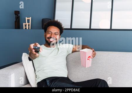 Ein lächelnder Mann, der zu Hause auf dem Sofa fernsieht Stockfoto