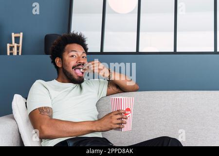 Ein Mann, der Popcorn isst und zu Hause auf dem Sofa sitzt Stockfoto