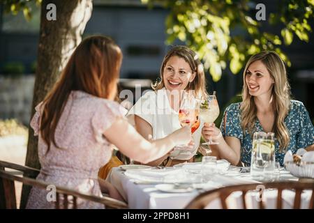 Fröhliche Freundinnen, die im Restaurant am Tisch auf Drinks toasten Stockfoto