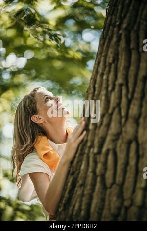 Glückliche Frau an Baum im Wald Stockfoto