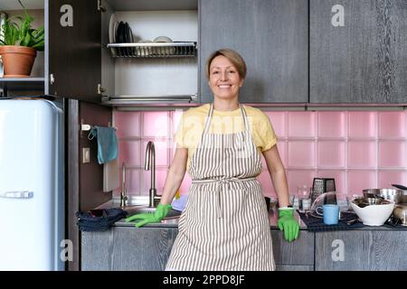 Glückliche Frau mit Schürze, die zu Hause in der Küche steht Stockfoto
